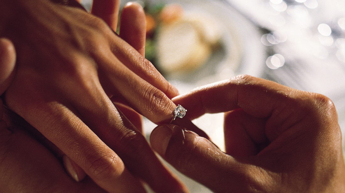 Placing a round engagement ring on a finger after a proposal.